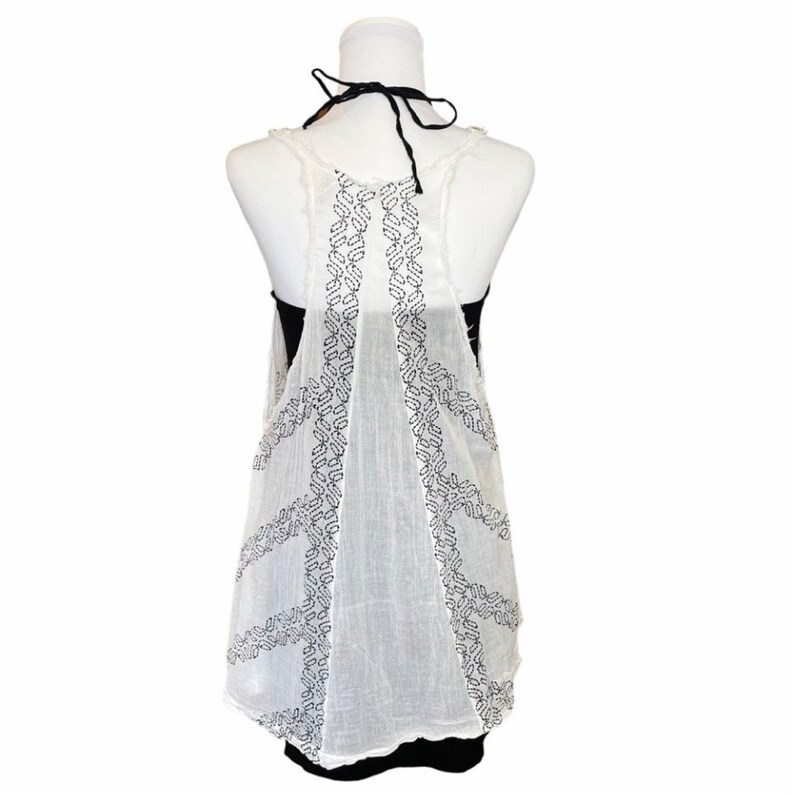 May include: White sleeveless top with black embroidered details. The top is sheer and has a loose, flowing fit.