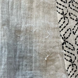 May include: A close-up of a white fabric with a black and white geometric pattern. The fabric is textured and has a slightly frayed edge.