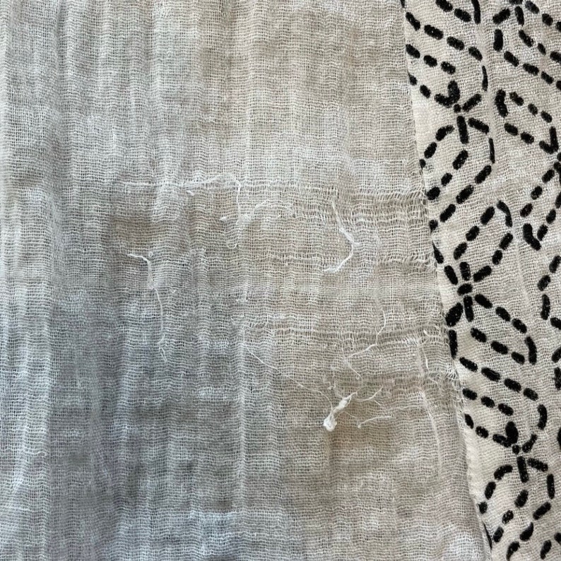 May include: A close-up of a white fabric with a black and white geometric pattern. The fabric is textured and has a slightly frayed edge.