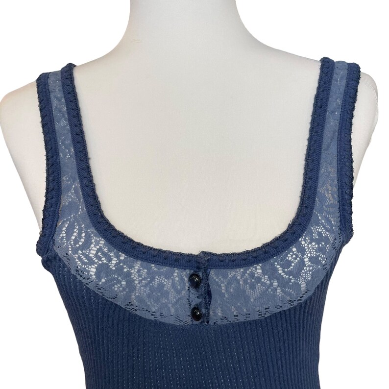 May include: A blue ribbed tank top with a lace trim and a single button closure at the neckline.
