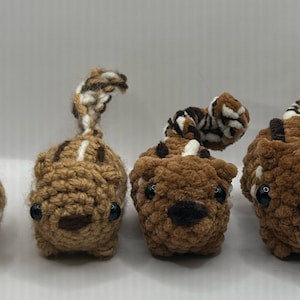 May include: Four crocheted stuffed squirrels in different sizes. The squirrels are brown and white with black eyes and noses. The squirrels are all facing forward.