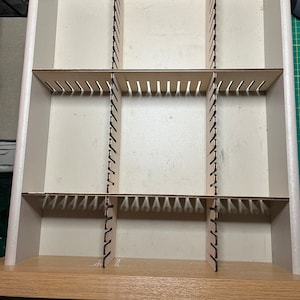 May include: A white drawer organizer with nine compartments. The organizer is made of wood and has a light brown finish. The compartments are separated by thin wooden dividers.