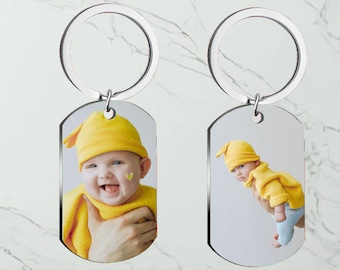 Könnte beinhalten: Zwei rechteckige Schlüsselanhänger mit silbernen Ringen. Jeder Schlüsselanhänger zeigt ein Farbfoto eines Babys mit gelbem Hut und Pullover. Ein Baby lächelt mit einem gelben Herzaufkleber auf der Wange.