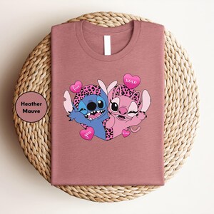 A pink t-shirt with a cartoon image of two cartoon characters, a blue character and a pink character, sitting together and smiling.