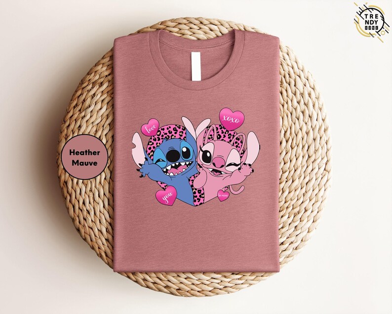 A pink t-shirt with a cartoon image of two cartoon characters, a blue character and a pink character, sitting together and smiling.