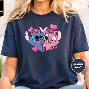 A person wearing a navy blue t-shirt with a graphic design featuring two cartoon characters, one blue and one pink, with hearts and the text "I love you" on them.