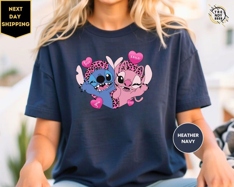 A person wearing a navy blue t-shirt with a graphic design featuring two cartoon characters, one blue and one pink, with hearts and the text "I love you" on them.