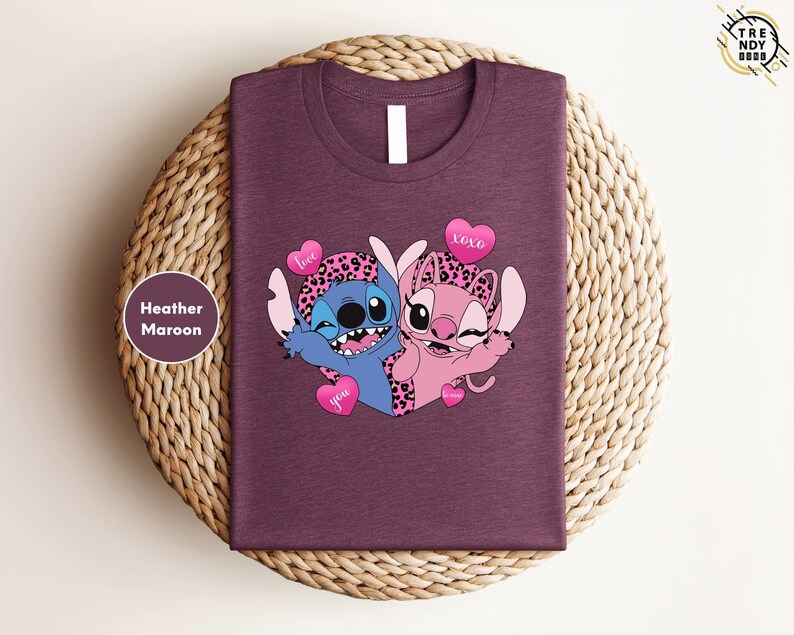 A purple t-shirt with a graphic design featuring two cartoon characters, a blue one and a pink one, along with hearts and the text "love you".