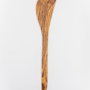 May include: A wooden spatula with a brown and olive wood grain pattern. The spatula has a rounded, slightly curved head and a long, thin handle.