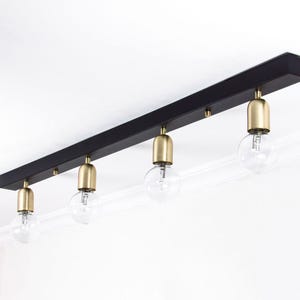 May include: A black ceiling light fitting with four brass-coloured bulb holders and clear, round light bulbs. The fitting is mounted on a white ceiling, showcasing a modern design.