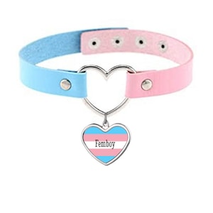May include: A pink and blue faux leather choker with a heart-shaped metal charm. The charm has a transgender pride flag design and the word "Femboy" printed on it.