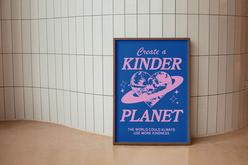 May include: A blue poster with the text "Create a Kinder Planet" in pink lettering. The poster features a pink heart-shaped planet with a ring around it. The text "The world could always use more kindness" is also included in pink lettering.