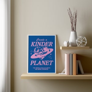 May include: A blue and pink poster with the text "Create a Kinder Planet" and a pink heart-shaped planet with a ring around it. The text below the planet reads "The world could always use more kindness."