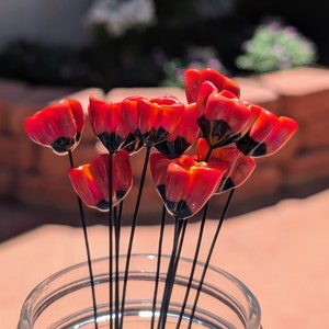 May include: A glass jar filled with a bouquet of red and black artificial flowers. The flowers have a tulip-like shape with red petals and black accents. The stems are thin and black. The jar is clear and sits on a light-colored surface.