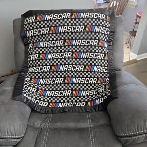 Kocyk polarowy do łóżeczka dziecięcego z logo Nascar na czarno-białym tle w kratkę i pasującą czarną satynową lamówką.