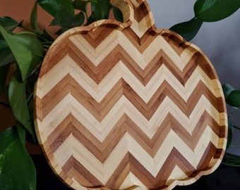 May include: A wooden serving tray shaped like a pumpkin with a chevron pattern in shades of brown and beige.