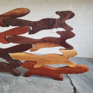 K&ouml;nnte beinhalten: Eine Wanddekoration aus Holz, die aus mehreren Holzst&uuml;cken in verschiedenen Braunt&ouml;nen besteht. Die St&uuml;cke sind in einer kaskadierenden Anordnung angeordnet, die an eine Reihe springender Tiere erinnert.