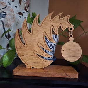 May include: A wooden Christmas tree ornament holder with a natural wood finish. The holder is shaped like a stylised tree with a round ornament hanging from the top. The holder is sitting on a wooden base.