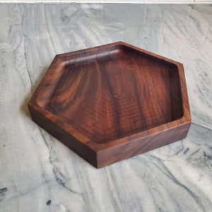May include: A hexagonal wooden tray made of dark walnut wood. The tray has a smooth, polished finish and is perfect for serving snacks or holding small items.