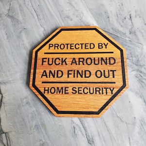 May include: A wooden sign with black text that reads "Protected by Fuck Around and Find Out Home Security". The sign is shaped like an octagon and has a wood grain pattern.
