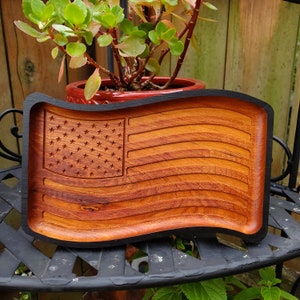 May include: A wooden tray carved in the shape of an American flag. The tray is made of dark wood with a natural wood finish. The stars and stripes are carved into the wood.