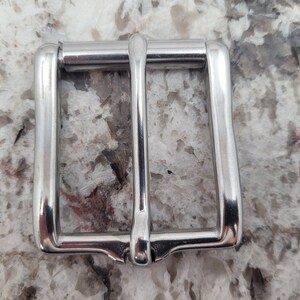 May include: A silver metal belt buckle with a smooth, polished finish.