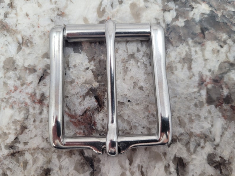 May include: A silver metal belt buckle with a smooth, polished finish.