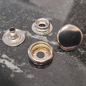 May include: Three silver metal snap fasteners, one with a raised center, one with a flat top, and one with a gold center.