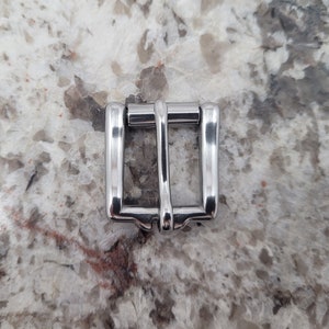 May include: A silver metal buckle for a belt or strap.