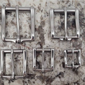 May include: Four silver metal belt buckles of different sizes. The buckles are all rectangular with a smooth, polished finish.