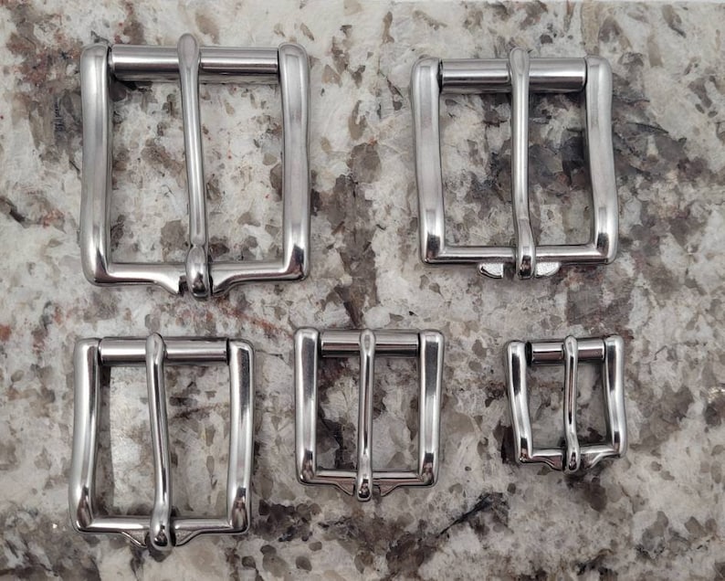 May include: Four silver metal belt buckles of different sizes. The buckles are all rectangular with a smooth, polished finish.
