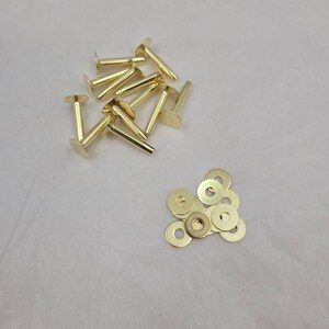 May include: A pile of gold-colored metal rivets and a pile of gold-colored metal washers.