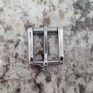 May include: A silver metal buckle for a belt or strap.