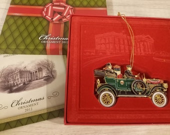 May include: A red box with a green and gold Christmas ornament inside. The ornament is a gold car with three people inside. The box has the text "The White House Historical Association" and "Christmas Ornament 2012" on it.