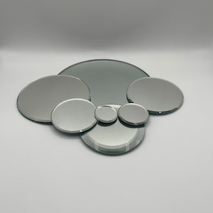 May include: A set of six round, silver-toned mirrors of varying sizes. The mirrors are arranged in a cluster, with the largest mirror in the center and the smaller mirrors surrounding it.