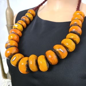 May include: A necklace made of large, round, amber-colored beads. The beads are strung on a brown cord and have a natural, rustic look.