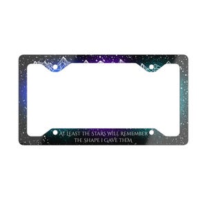 May include: License plate frame with a starry night design in shades of blue, purple, and teal. The frame features a mountain range silhouette and the text "AT LEAST THE STARS WILL REMEMBER THE SHAPE I GAVE THEM."