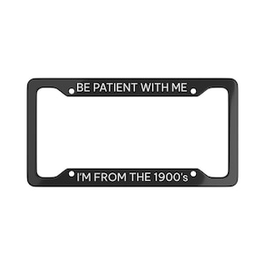 May include: Black license plate frame with white text that reads "BE PATIENT WITH ME" at the top and "I'M FROM THE 1900's" at the bottom. The frame has a rectangular shape.