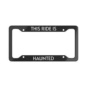 Può includere: Cornice nera per targa con la scritta bianca "THIS RIDE IS HAUNTED". La cornice ha una forma rettangolare con angoli arrotondati e fori di montaggio.