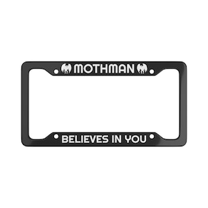 Puede incluir: Marco de matrícula negro con texto blanco. La parte superior dice "MOTHMAN" con un gráfico de polilla a cada lado, y la parte inferior dice "BELIEVES IN YOU".