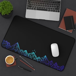 Könnte beinhalten: Eine schwarze Mausmatte mit einem blauen und violetten geometrischen Bergdesign. Die Mausmatte liegt auf einer grauen Oberfläche mit einem Laptop, einem Notizbuch und einer Tasse Kaffee.