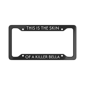 Pode incluir: Moldura preta para placa de carro com texto branco. O texto diz "THIS IS THE SKIN" na parte superior e "OF A KILLER BELLA" na inferior. A moldura é retangular com cantos arredondados.