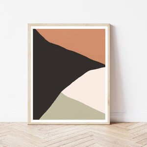 Może przedstawiać: Abstrakcyjny wydruk artystyczny w drewnianej ramie. Grafika przedstawia geometryczne kształty w kolorach czarnym, brzoskwiniowym, ecru i oliwkowym. Wydruk jest prezentowany na białej ścianie i drewnianej podłodze.