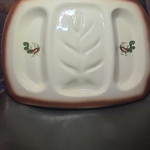 May include: Cream-colored ceramic serving platter with a brown rim and two side compartments. The center has a leaf design, and each side features a small, colorful bird illustration. A vintage-style piece.