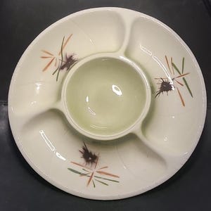 Puede incluir: Plato de cerámica blanco roto con un cuenco central y cuatro compartimentos. Decorado con diseños abstractos en marrón, verde y naranja. Una pieza vintage para servir aperitivos o entremeses.