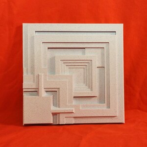 May include: A square, off-white, geometric wall art piece with a layered, recessed design. The artwork features a series of nested squares and rectangular shapes, creating a three-dimensional effect. The background is a solid, bright orange.