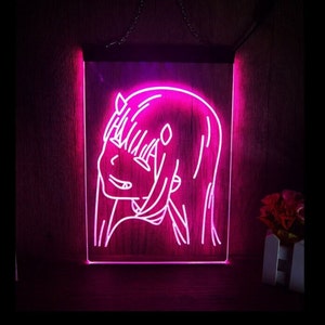Könnte beinhalten: Pinkfarbenes Neon-Schild mit einer Strichzeichnung eines Anime-Charakters mit langen Haaren und Hörnern. Der Charakter lächelt und blickt nach rechts. Das Schild befindet sich auf einem hölzernen Hintergrund.