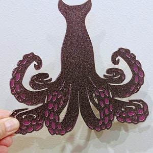 May include: A brown glitter octopus with pink accents. The octopus has eight tentacles with suction cups.
