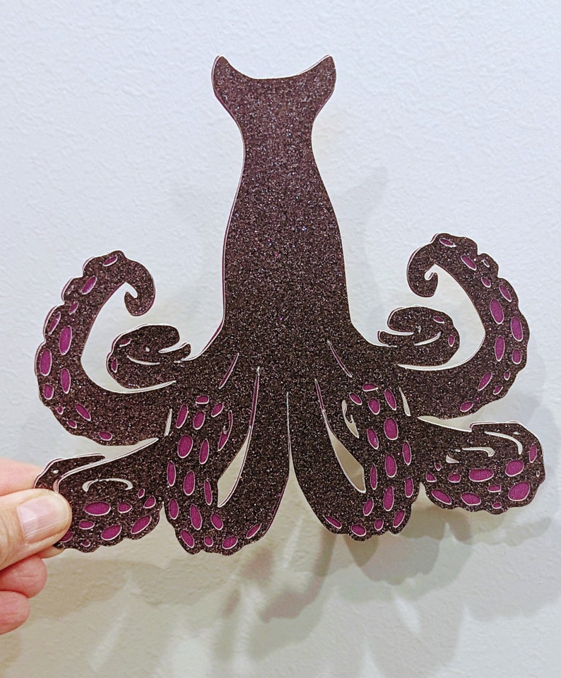 May include: A brown glitter octopus with pink accents. The octopus has eight tentacles with suction cups.