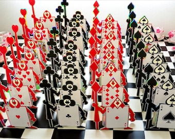 May include: A set of decorative playing card figures arranged on a black and white checkered board. The figures feature various suits including hearts, clubs, diamonds, and spades, each with a distinct character design and a tall staff held by the figure.